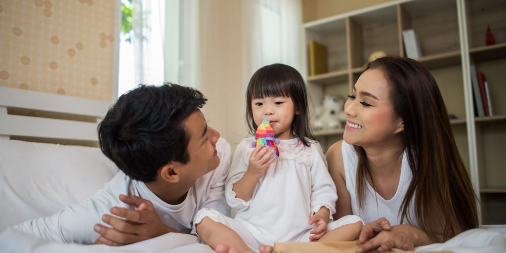 Happy child with parents playing in the bed at home